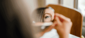 Femme se regardant dans un petit miroir, on aperçoit une partie de son visage. Réflexion sur la relation à son image personnelle