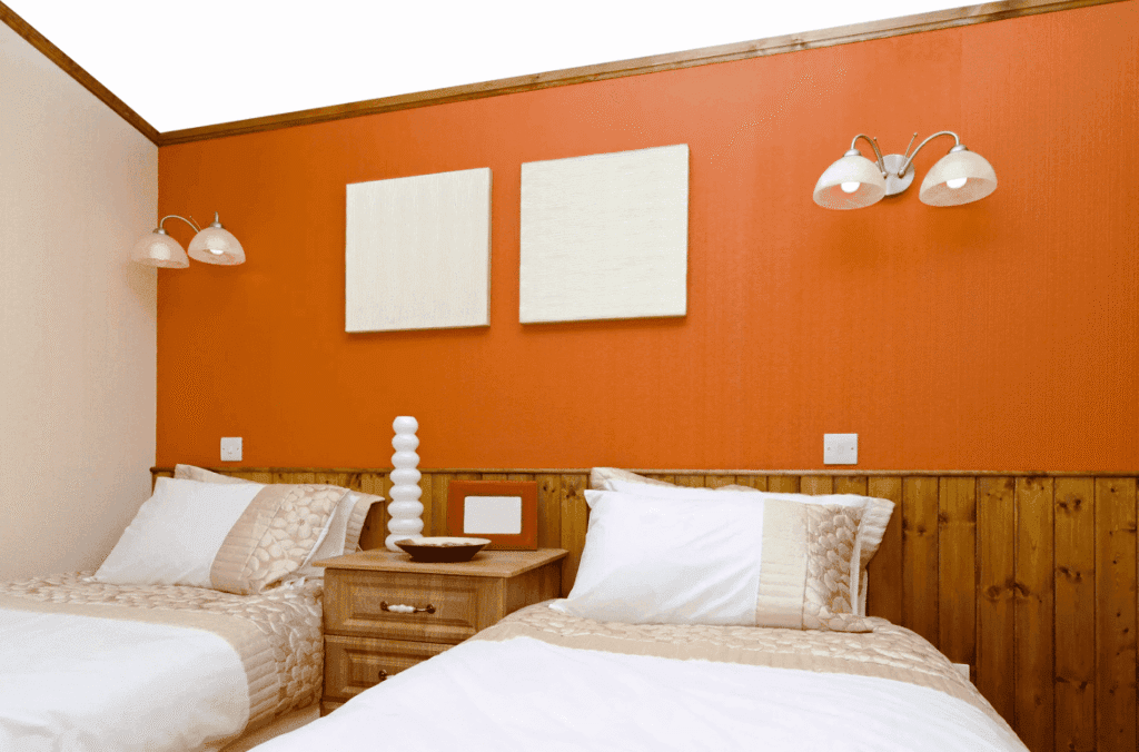 Chambre avec deux lits simples et un mur peint en orange vif, illustrant la sensation psychologique de chaleur liée aux couleurs chaudes.