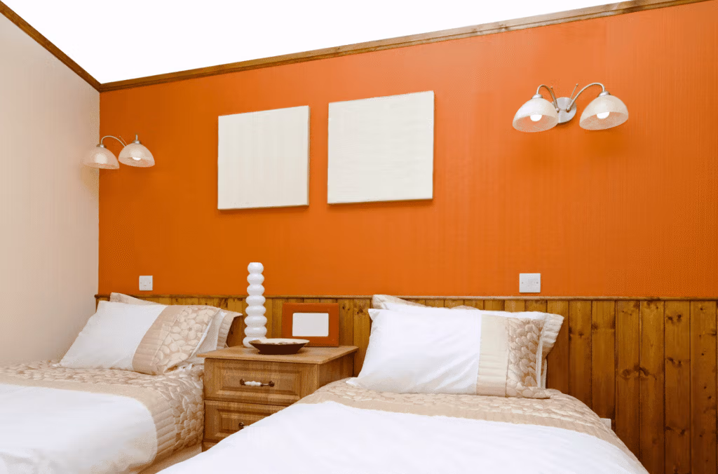 Chambre avec deux lits simples et un mur peint en orange vif, illustrant la sensation psychologique de chaleur liée aux couleurs chaudes.