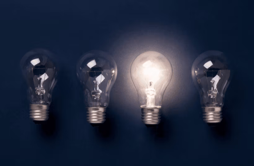 Quatre ampoules posées côte à côte, dont une seule est allumée tandis que les trois autres sont éteintes.