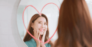 Femme enthousiaste se regardant dans un miroir décoré d’un cœur dessiné.