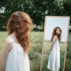 Femme en robe blanche se regardant dans un miroir, réfléchissant à son image.