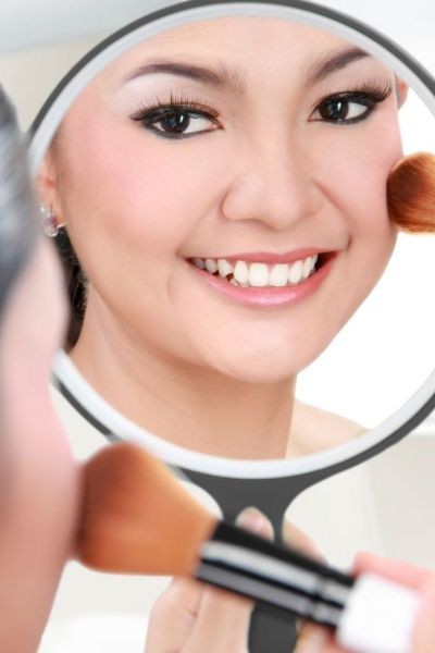femme asiatique se poudrant le teint en se regardant dans un miroir
