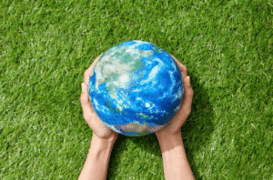 Mains tenant un globe terrestre posé dans l’herbe verte.