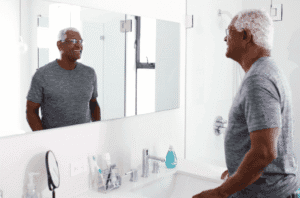 Homme souriant se regardant dans le miroir de sa salle de bain.